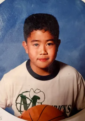 Herman as a boy in a Mavericks T-shirt, holding a basketball