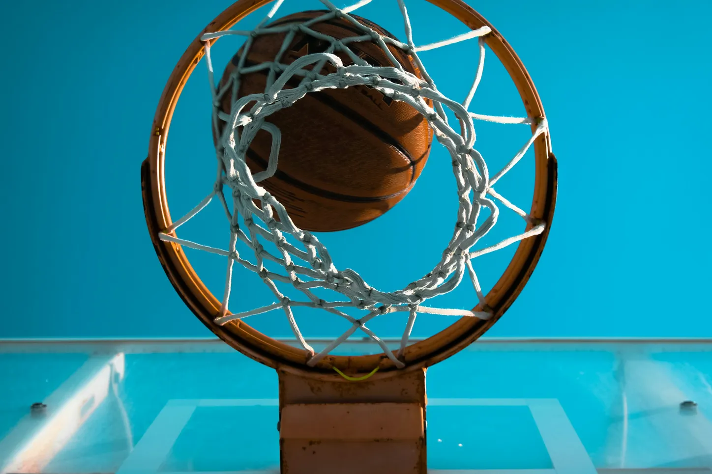 A basketball dropping through the net against a teal sky